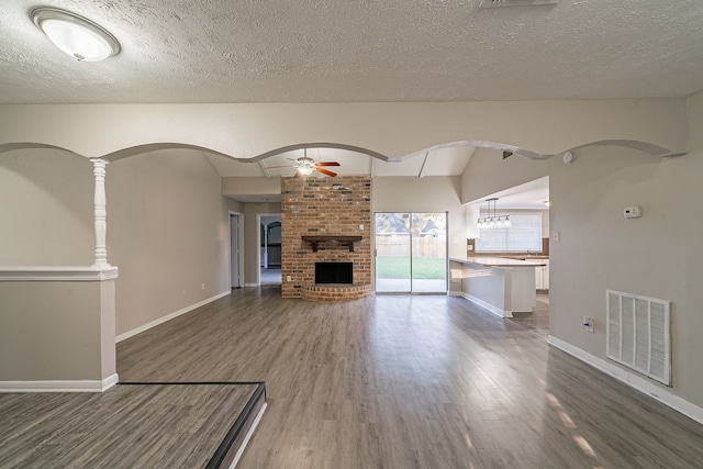 unfurnished living room with visible vents, ceiling fan, dark wood-type flooring, vaulted ceiling, and a fireplace