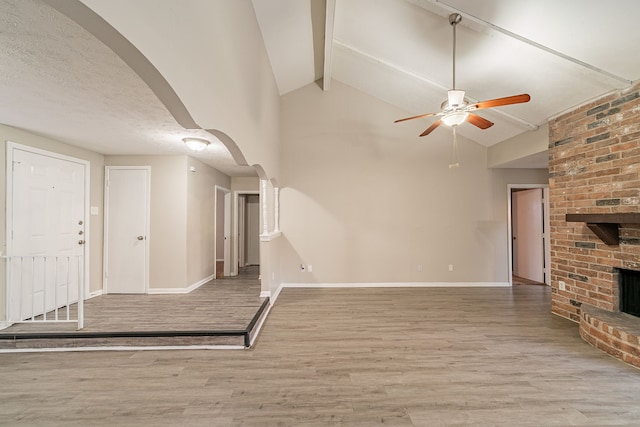 unfurnished living room featuring arched walkways, a fireplace, baseboards, and wood finished floors