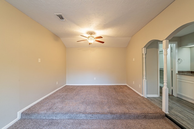 empty room featuring arched walkways, carpet floors, visible vents, baseboards, and vaulted ceiling