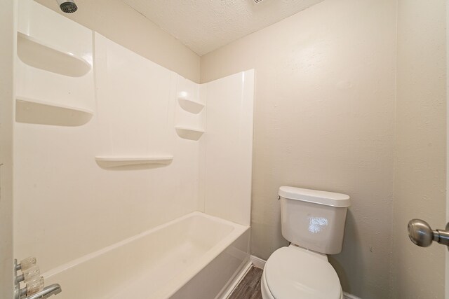 bathroom featuring baseboards, toilet, wood finished floors, a textured ceiling, and shower / bathtub combination