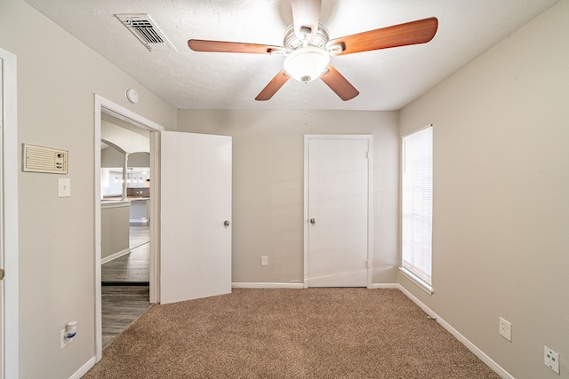 unfurnished bedroom with carpet, multiple windows, visible vents, and a textured ceiling