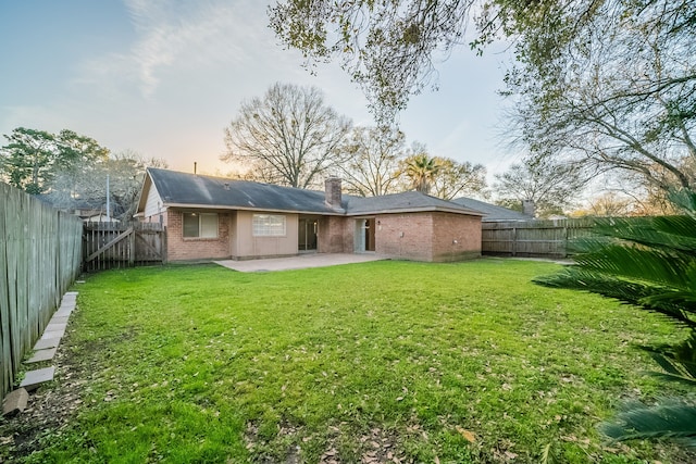 back of property featuring a fenced backyard, a chimney, a yard, a patio area, and brick siding