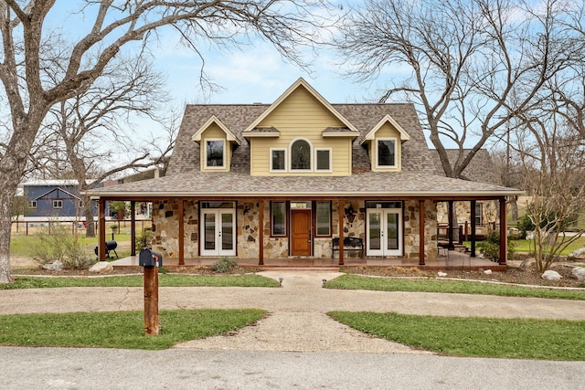 farmhouse inspired home featuring stone siding, french doors, roof with shingles, and covered porch