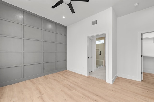 unfurnished bedroom featuring visible vents, a ceiling fan, wood finished floors, a walk in closet, and a decorative wall