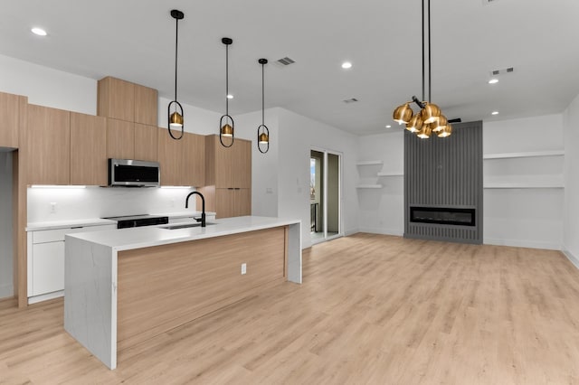 kitchen with modern cabinets, stainless steel microwave, light countertops, light wood-type flooring, and a sink