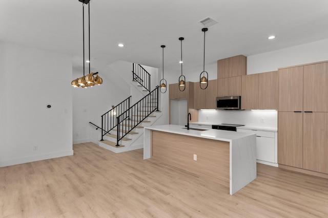 kitchen with a sink, light wood-style floors, light countertops, stainless steel microwave, and modern cabinets