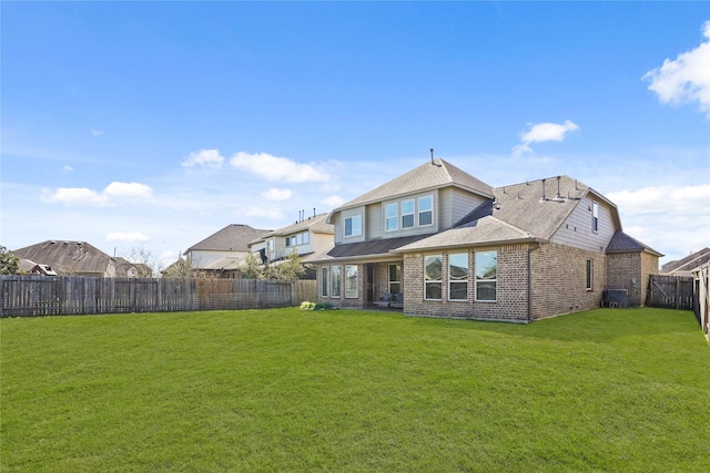 back of property with a shingled roof, a fenced backyard, a lawn, and brick siding