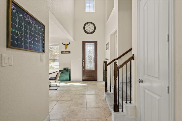 entryway with light tile patterned floors, stairs, a towering ceiling, and baseboards