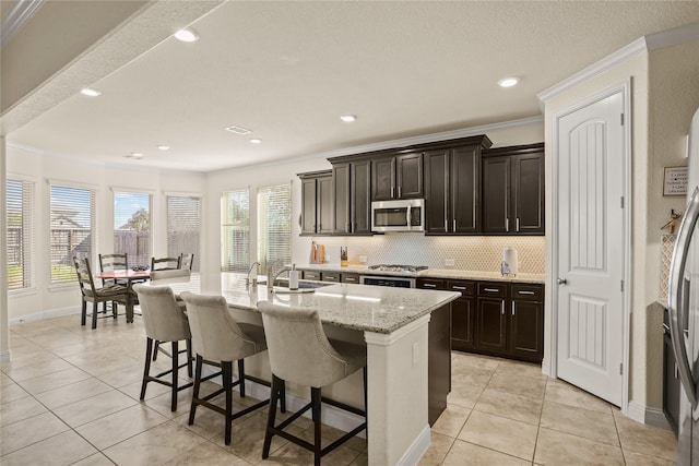 kitchen with crown molding, tasteful backsplash, stainless steel microwave, a sink, and a kitchen breakfast bar