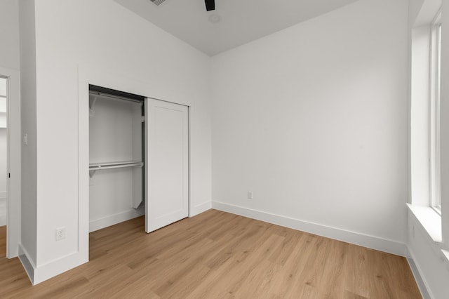 unfurnished bedroom with light wood-type flooring, a closet, multiple windows, and baseboards