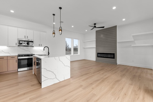 kitchen with a fireplace, light wood finished floors, stainless steel appliances, backsplash, and a sink