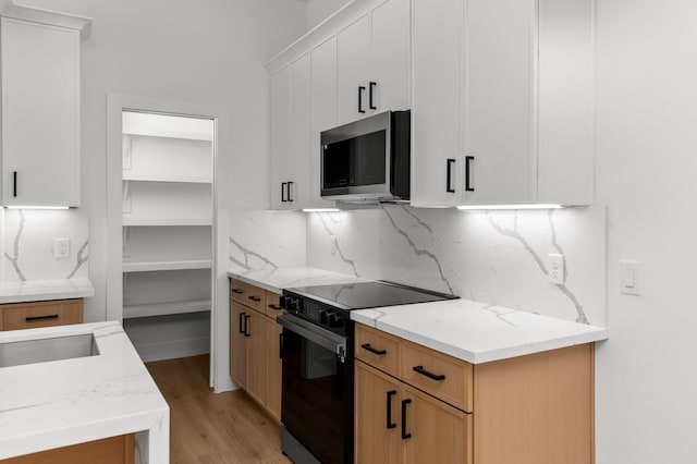 kitchen with tasteful backsplash, light wood-style flooring, stainless steel microwave, black electric range, and white cabinetry