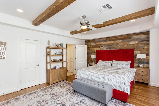 bedroom with wooden walls, wood finished floors, visible vents, an accent wall, and beamed ceiling