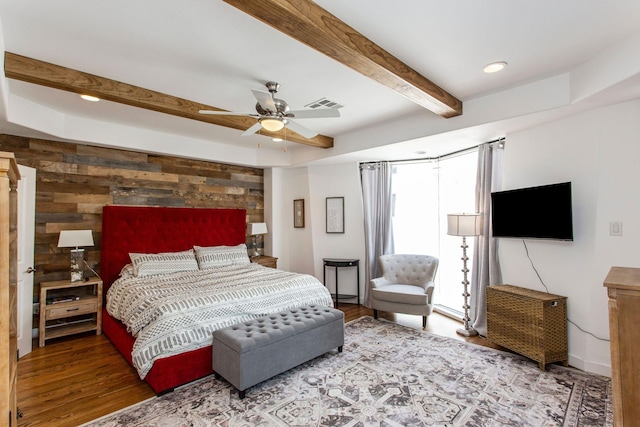 bedroom featuring visible vents, wooden walls, an accent wall, beam ceiling, and wood finished floors