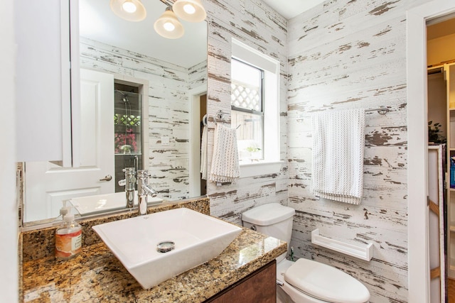 bathroom with toilet, vanity, and wallpapered walls