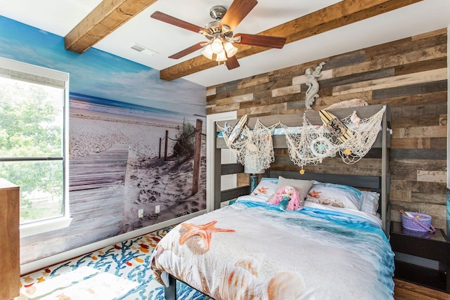 bedroom with visible vents, wooden walls, beamed ceiling, and a ceiling fan