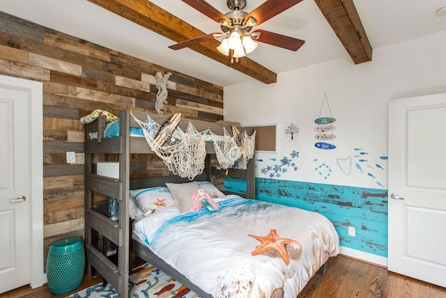 bedroom with beamed ceiling, a ceiling fan, wood finished floors, wooden walls, and baseboards