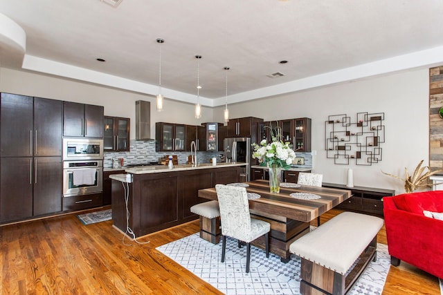 kitchen with dark wood finished floors, light countertops, wall chimney range hood, and appliances with stainless steel finishes