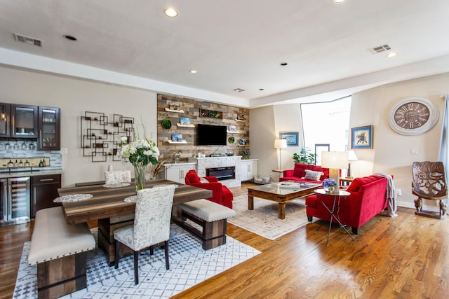 living room with a glass covered fireplace, wood finished floors, beverage cooler, and visible vents