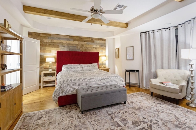 bedroom with beamed ceiling, visible vents, wood finished floors, wood walls, and an accent wall