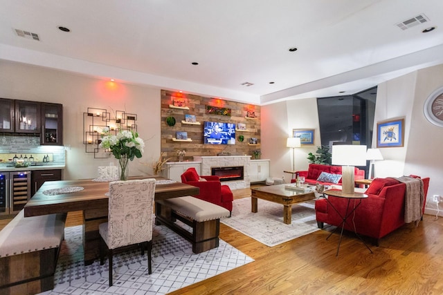 living area with wine cooler, visible vents, light wood-style floors, and a glass covered fireplace