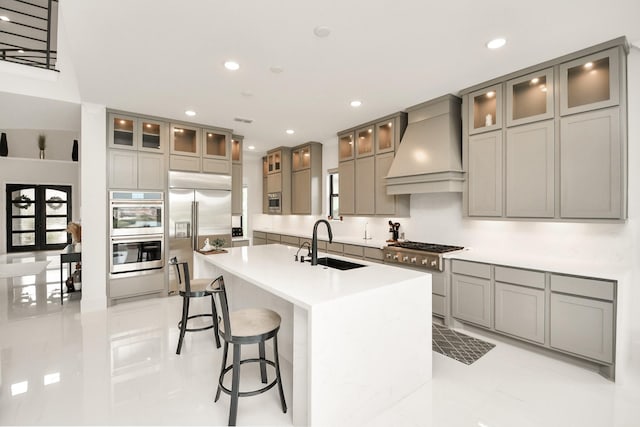 kitchen featuring gray cabinets, premium range hood, a sink, and built in appliances