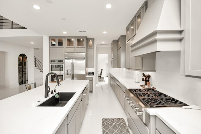 kitchen featuring custom range hood, appliances with stainless steel finishes, a sink, and gray cabinetry