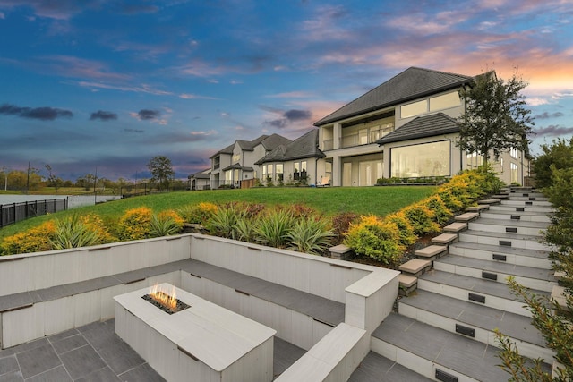 patio terrace at dusk featuring an outdoor fire pit and a lawn