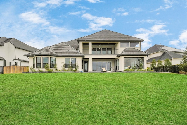 rear view of property with a yard, a balcony, and fence