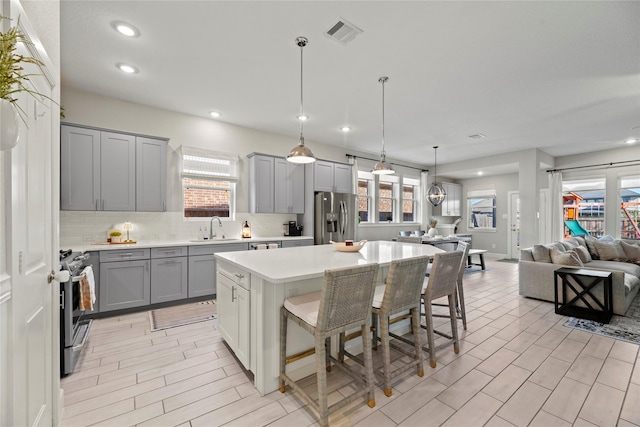 kitchen with stainless steel appliances, gray cabinets, visible vents, a sink, and a kitchen island