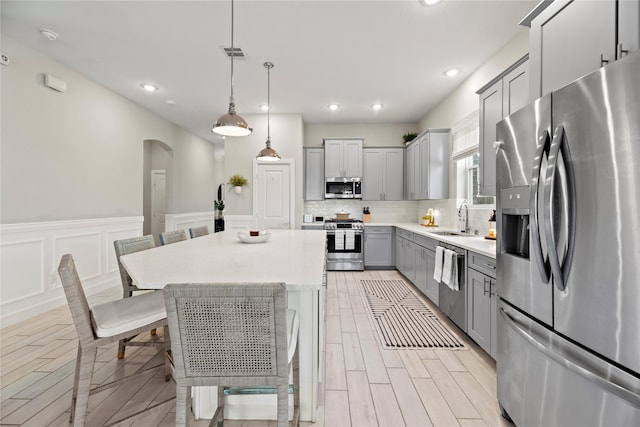 kitchen featuring arched walkways, gray cabinets, light countertops, decorative backsplash, and appliances with stainless steel finishes