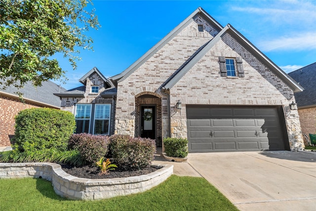 french country inspired facade with a garage, concrete driveway, and brick siding