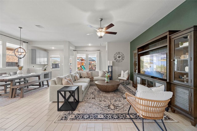 living area with light wood-type flooring, visible vents, and ceiling fan with notable chandelier