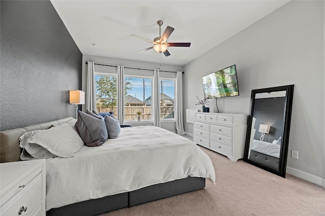 bedroom featuring baseboards, ceiling fan, a textured wall, and light colored carpet