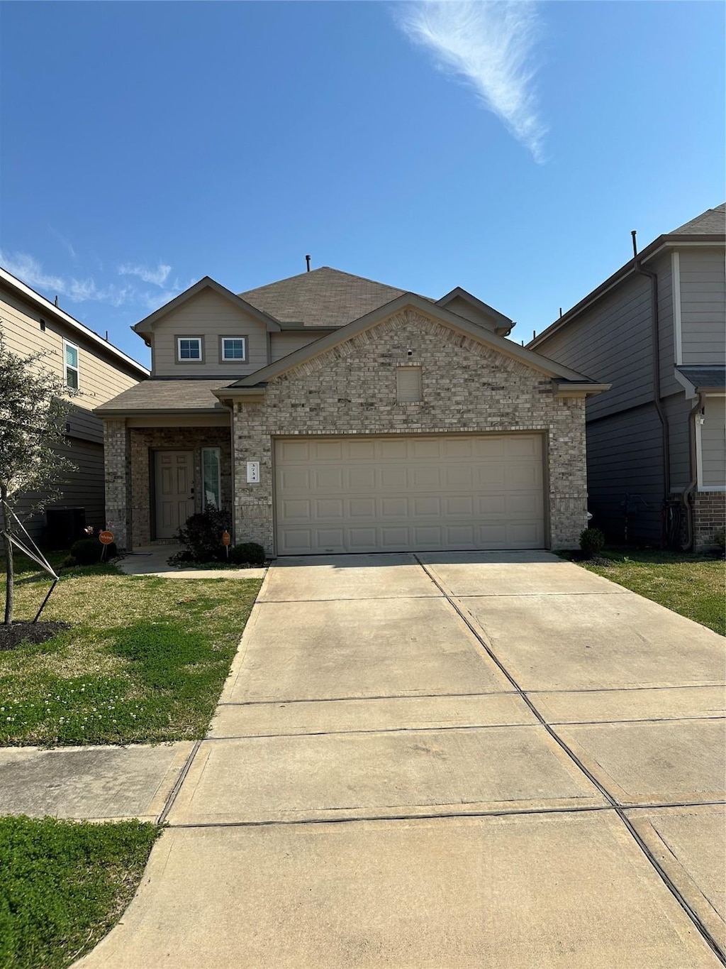 view of front facade with a front yard, driveway, a shingled roof, a garage, and brick siding