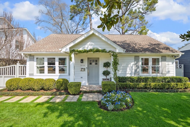 view of front of home with a front lawn, a shingled roof, and fence