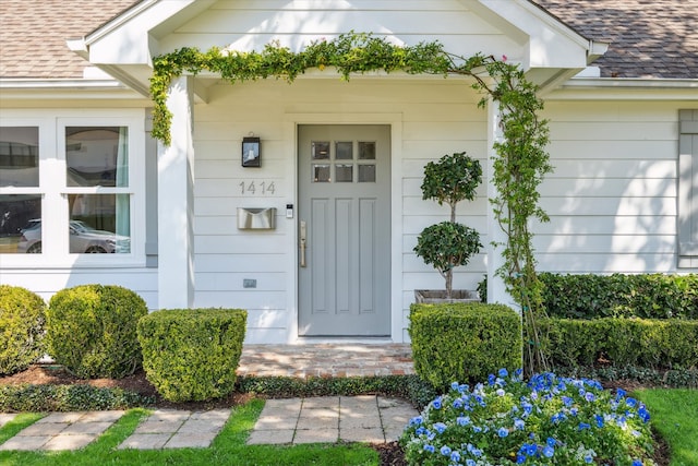 view of exterior entry with roof with shingles