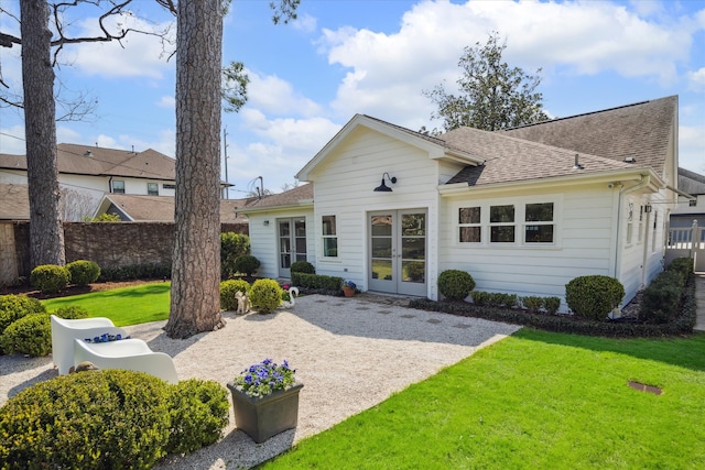 rear view of house with a shingled roof, french doors, a yard, and fence