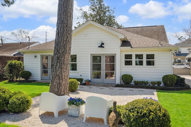 view of front of home with french doors, roof with shingles, a front lawn, and fence