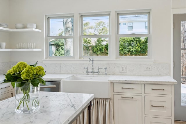 kitchen featuring light stone counters, white cabinets, and a sink