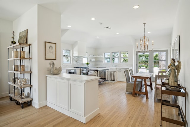 kitchen with light wood finished floors, light countertops, wall chimney range hood, high end stove, and a peninsula