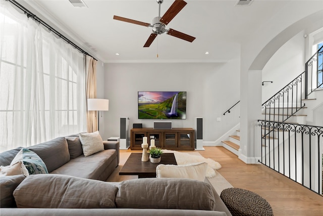 living area with arched walkways, crown molding, light wood finished floors, baseboards, and stairs