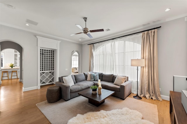 living area with arched walkways, visible vents, crown molding, and light wood finished floors