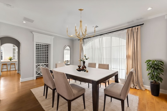 dining space with arched walkways, a chandelier, light wood-style flooring, baseboards, and crown molding