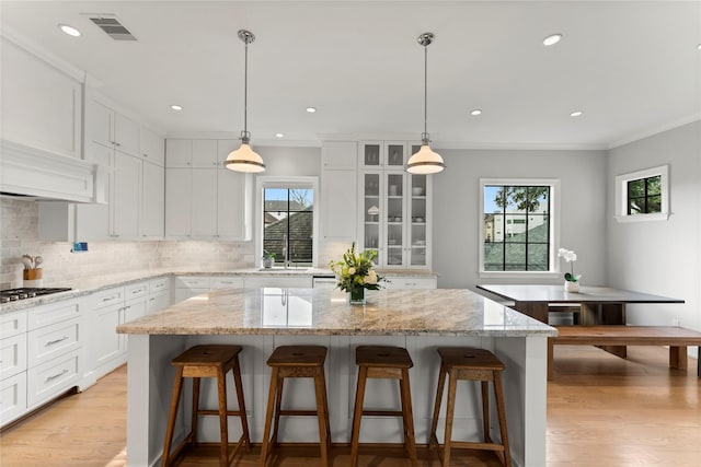 kitchen with white cabinetry, a kitchen breakfast bar, visible vents, backsplash, and a center island