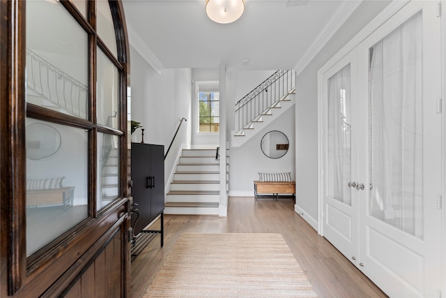 entrance foyer featuring light wood-style floors, crown molding, stairway, and baseboards