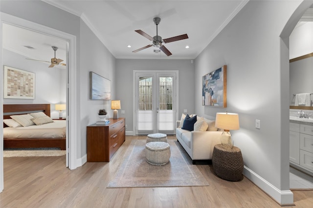 sitting room with light wood-style floors, baseboards, arched walkways, and crown molding