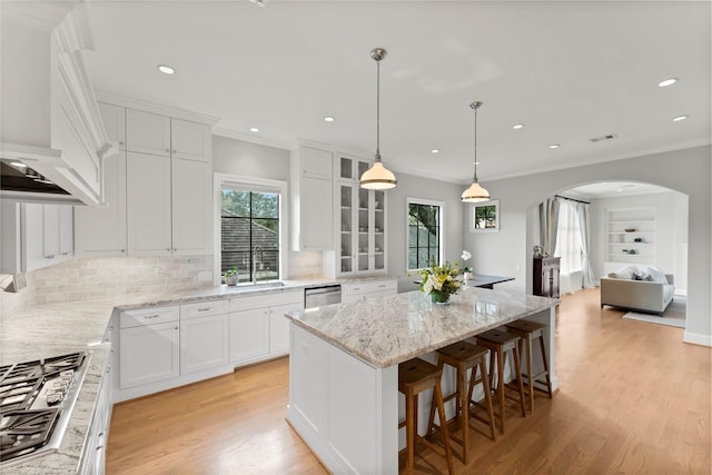 kitchen featuring arched walkways, a kitchen island, custom range hood, stainless steel appliances, and a sink