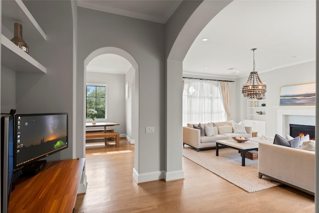 living room with a warm lit fireplace, baseboards, arched walkways, ornamental molding, and wood finished floors