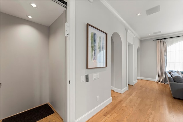 hallway featuring light wood-style floors, baseboards, arched walkways, and crown molding